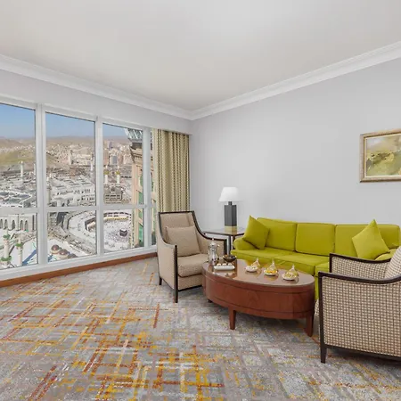 فندق سويس اوتيل المقام مكة المظهر الخارجي الصورة The image shows a well-furnished hotel room or suite. It features a cozy sitting area with a light green sofa and two armchairs, accompanied by a round wooden coffee table. There are decorative elements such as small bowls or trays on the table. The 